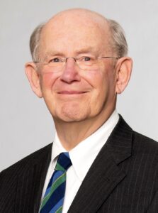 Bob Sink is a white man with grey hair. He is pictured smiling with his mouth closed. He wears a white shirt, a dark tie and a black jacket.