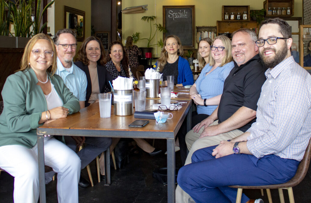 Ashley is pictured sitting down at a table with eight members of the staff from the Asheville office.