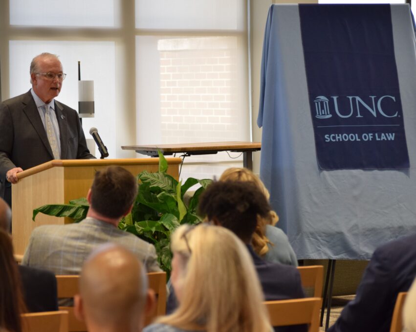 Dave Boliek, a white man with grey hair, stands at the podium to the left of the veiled portrait.