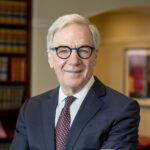 Reid, a white man with white hair, wears a white shirt, dark grey suit, burgundy tie, and glasses.