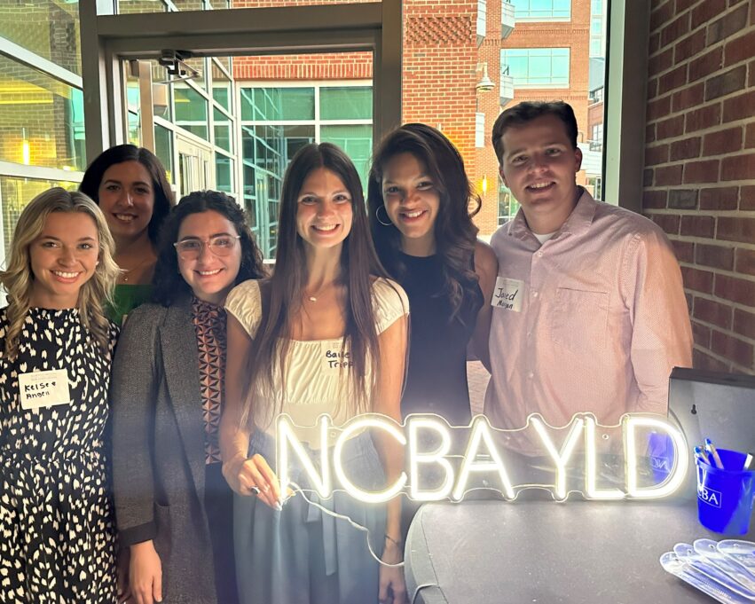 A group of six law students stands behind an "NCBA YLD" sign on a table.