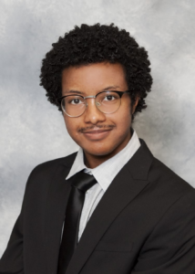 Melo, a Black man with dark brown curly hair, wears a white shirt, black tie, and black jacket.