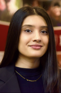 Shereena, a woman with dark brown hair, wears a black blouse and black jacket.