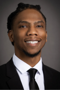 Zachary, a Black man with black hair, wears a white shirt, black tie and black jacket.