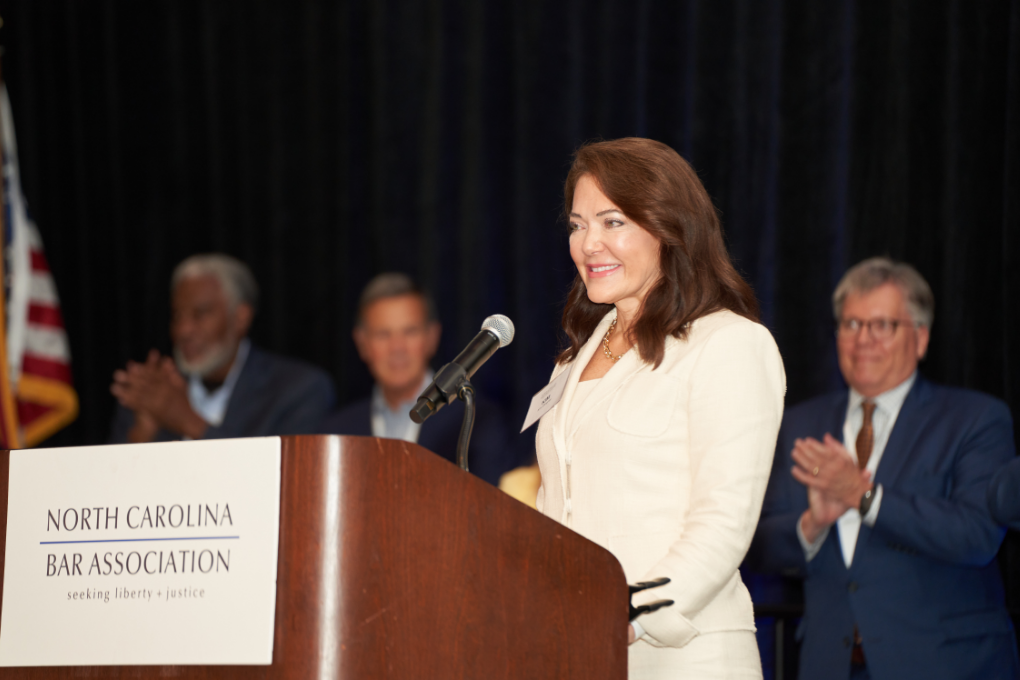 Kim, a white woman with brown hair, wears a cream-colored blouse and cream suit.