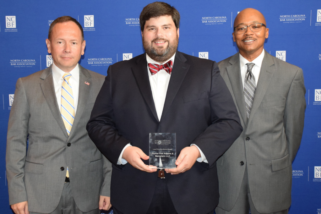 Michael, center, is a man with dark brown hair and a beard wearing a red bowtie, white shirt, and black suit. Jason is to his left and Clayton is to his right.