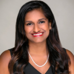 Manisha, a woman with dark brown hair, wears a black dress and string of pearls. 