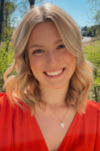 Recipient Emily Almond, a white college student with blond hair, wears an orange-red blouse and is smiling in a field.