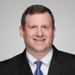 William, a white man with brown hair, wears a white shirt, blue tie, and black jacket. 