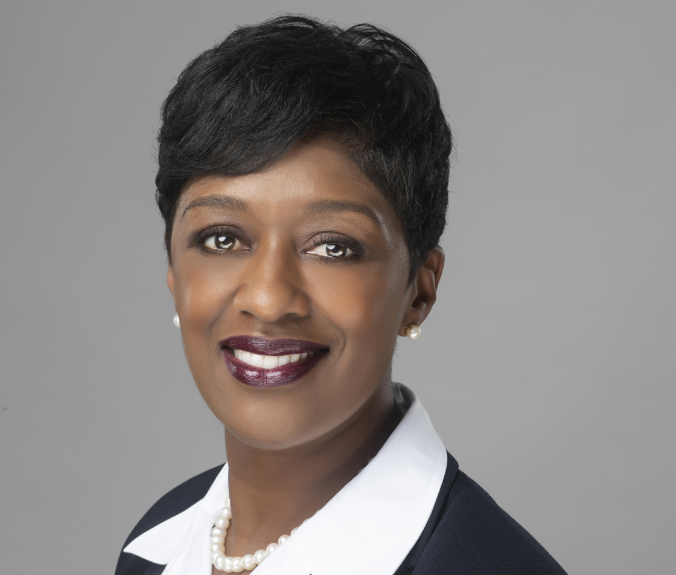 Afi, a Black woman with black hair, wears a white blouse, black blazer and pearl earrings and necklace.