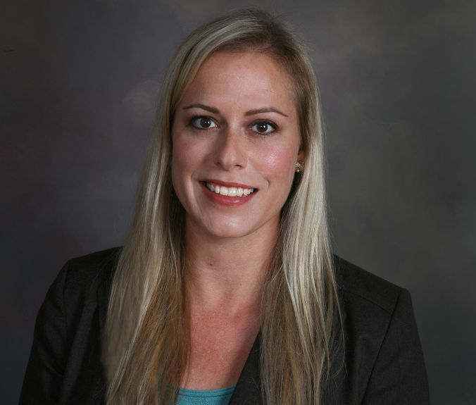 Katie, a white woman with blond hair, wears a teal blouse and black blazer.