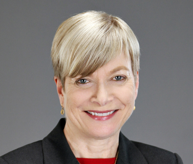 Susan, a white woman with blond hair, wears a red blouse and black jacket.