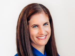 Colleen, a white woman with brown hair, wears a royal blue blouse.