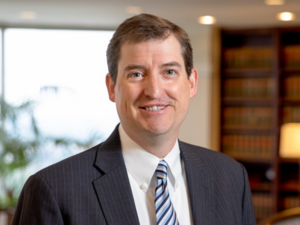 David, a white man with brown hair, wears a white shirt, blue and white striped tie, and grey pinstripe suit.