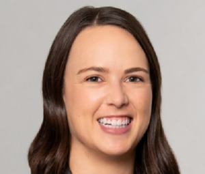 Andrea, a white woman with brown hair, wears a pink blouse and grey jacket.