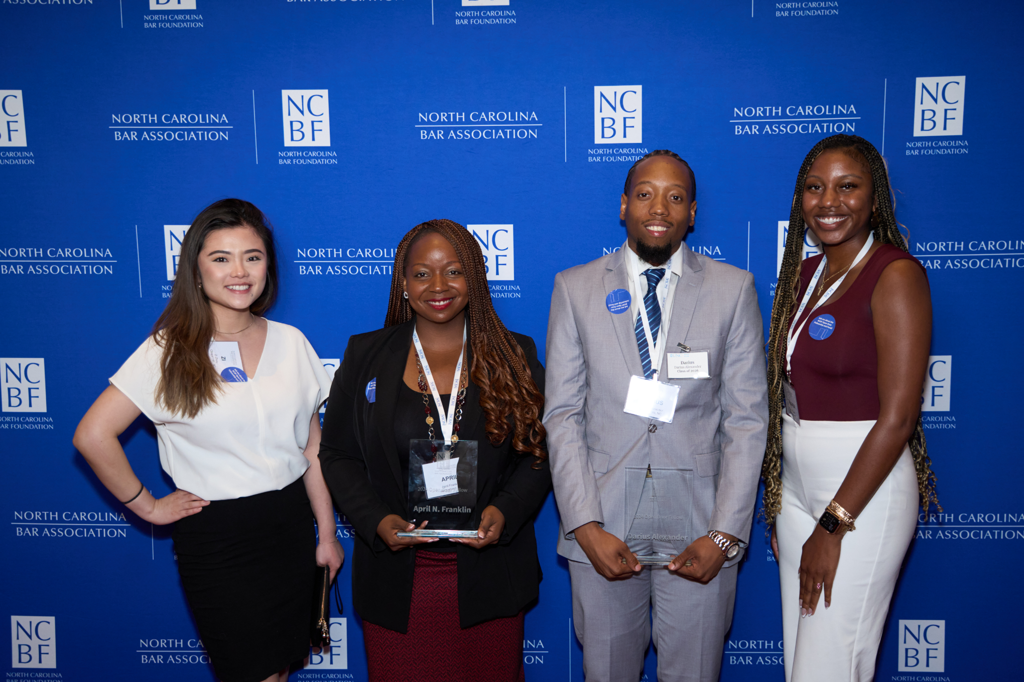 The fellows are pictured smiling and standing against an NCBF backdrop. Zi Yi is an Asian woman with brown hair wearing a white blouse and black skirt, April Franklin is a Black woman wearing a black blouse, black blazer and burgundy skirt, Darius Alexander is a Black man with black hair wearing a white shirt, blue tie, and grey suit, and Tavaria Smith is a Black woman with black hair wearing a burgundy blouse and white pants.