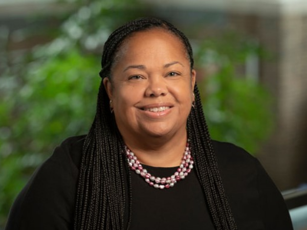 Alison Ashe-Card, a Black woman with black hair, wears a black blouse and necklace with pink and white beads.