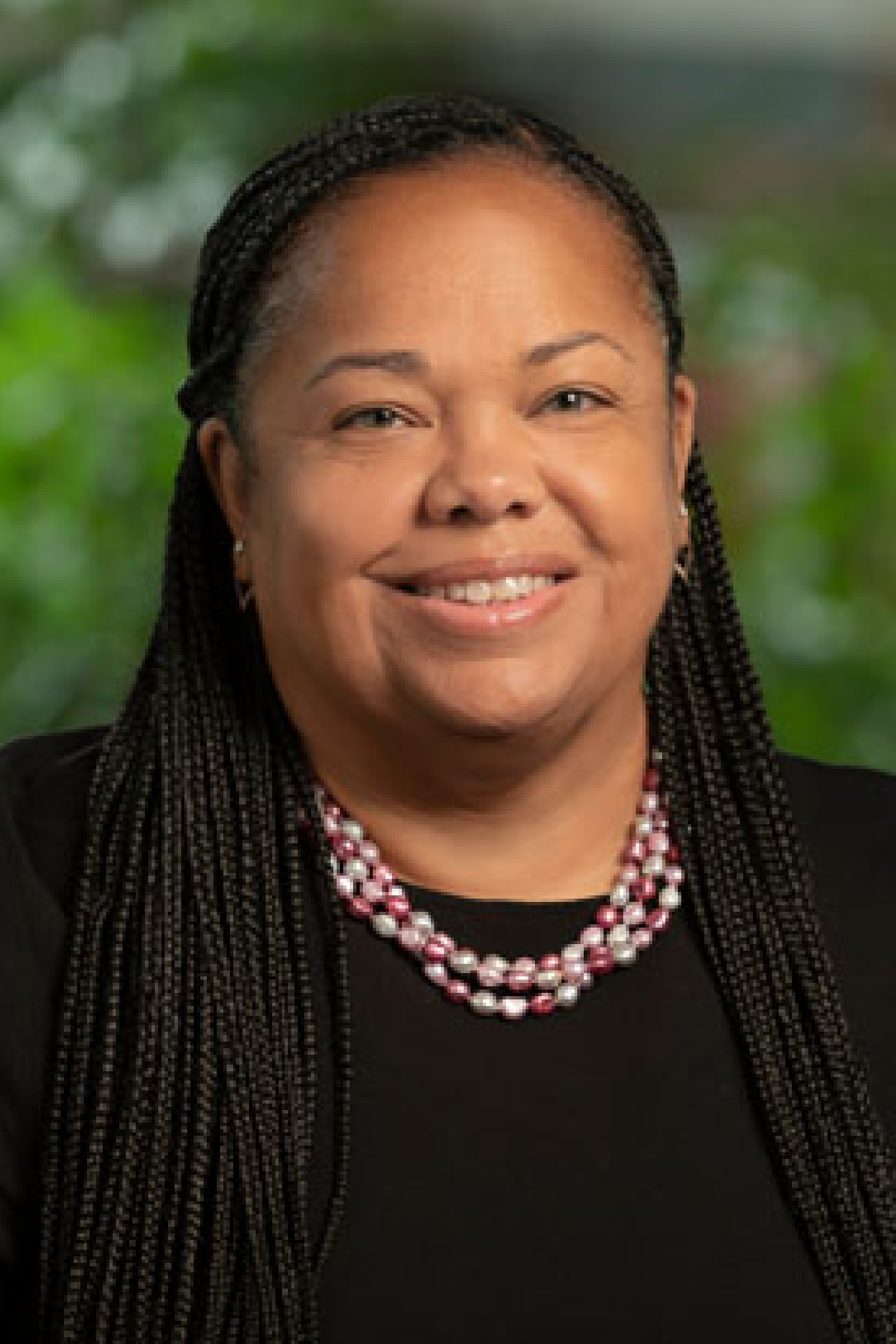 Alison Ashe Card is a Black woman with long black hair. She is wearing a black blouse and a pink and white beaded necklace.