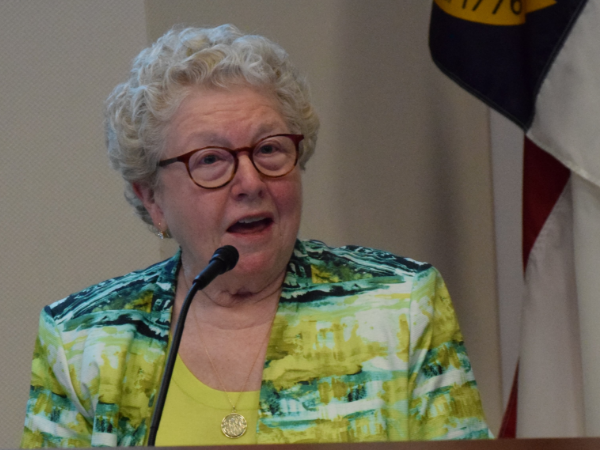 Catherine Arrowood, a white woman with white hair, wears a lime green shirt and blazer with yellow and green print.