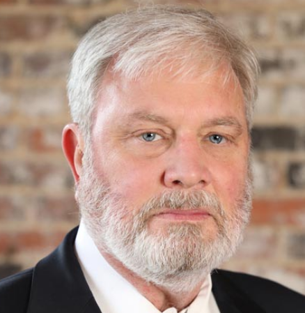 Kevin, a white man with white hair and a beard, wears a white shirt and a black blazer. 