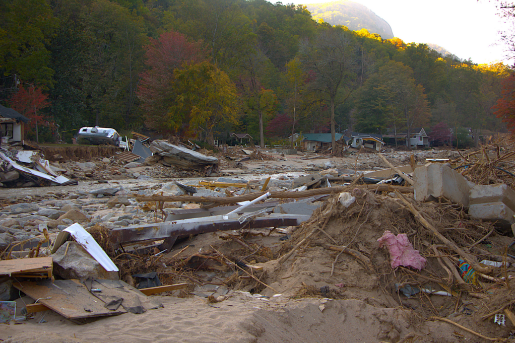 The aftermath of Helene is shown in this photo. Debris from trees, homes and cars is strewn across the landscape. Trees and some standing houses are visible in the background.